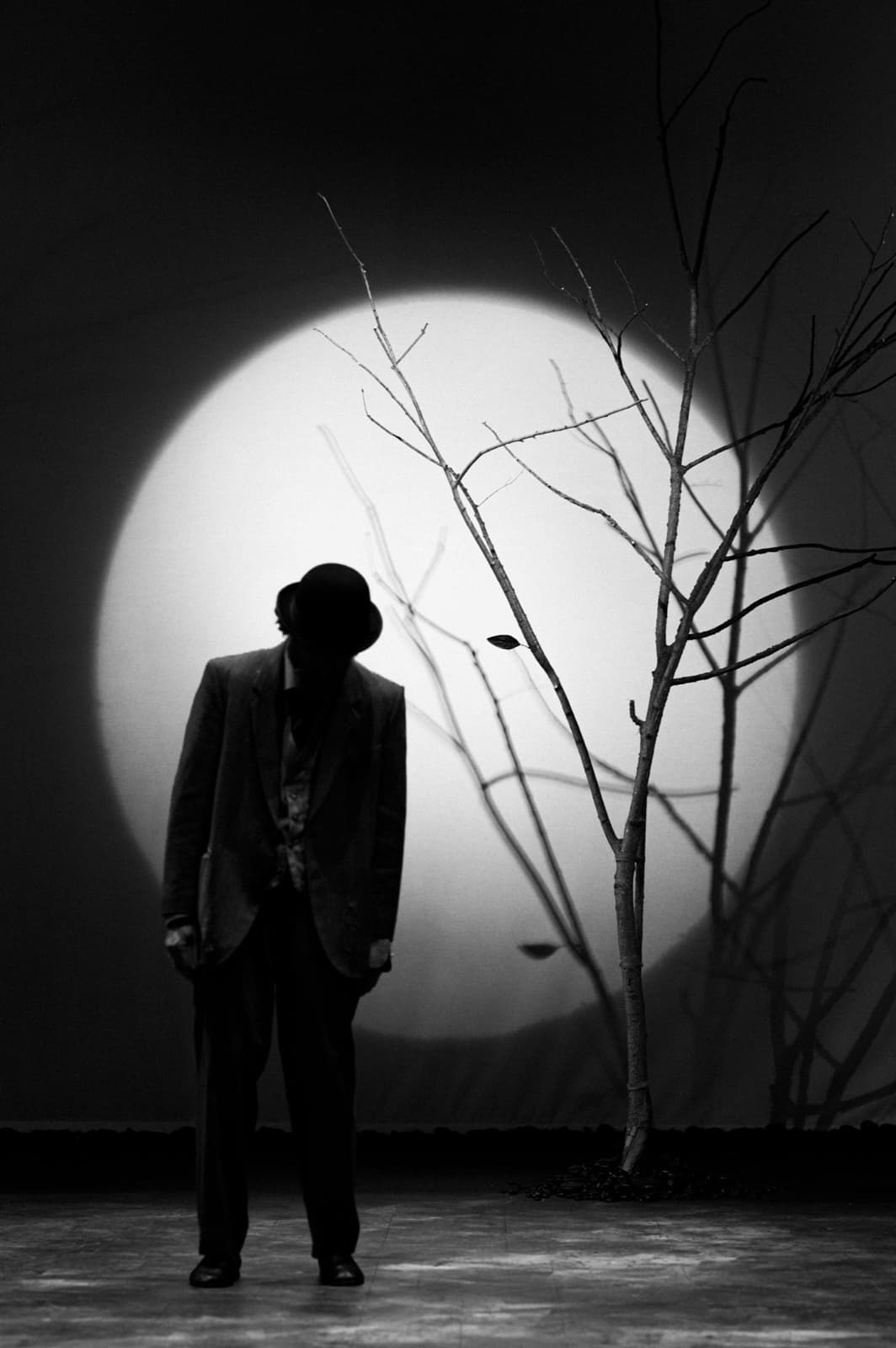 Vladimir in silhouette, head bowed, before a full moon and the bare tree