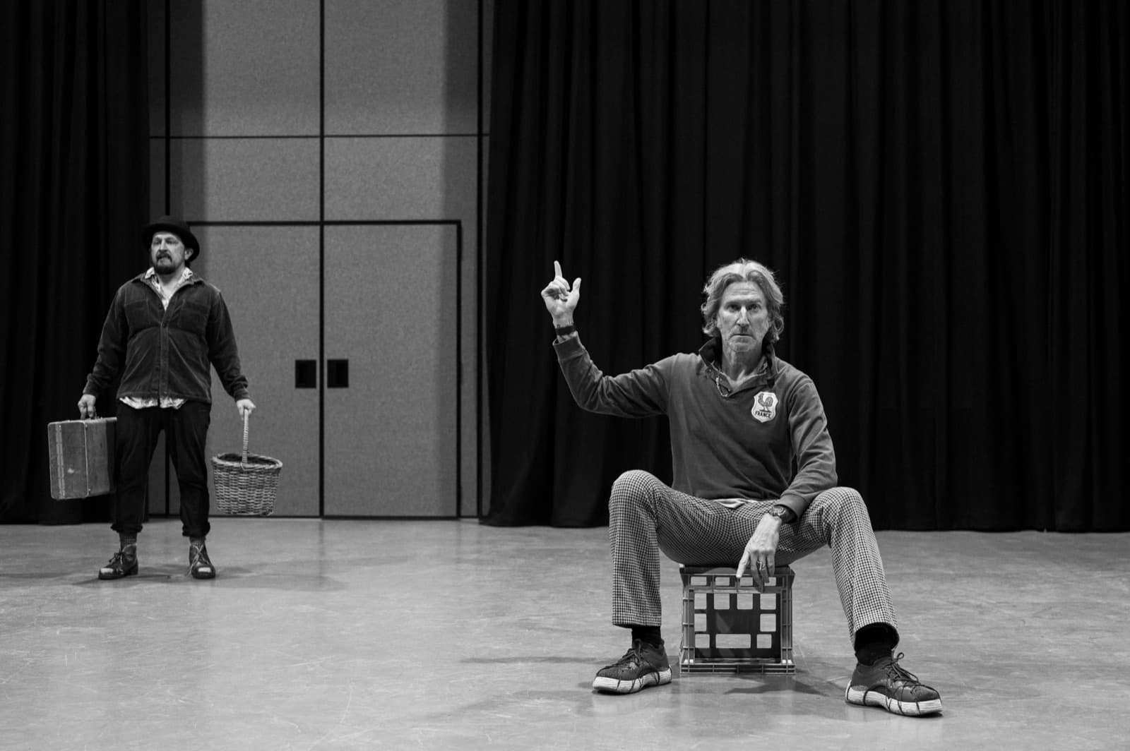 Pozzo seated on a milk crate with a raised finger, Lucky standing behind